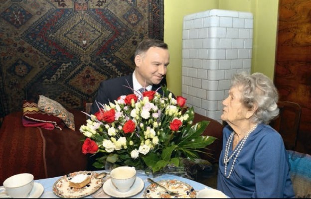Prezydent Andrzej Duda wręcza pani Wandzie bukiet biało-czerwonych kwiatów
