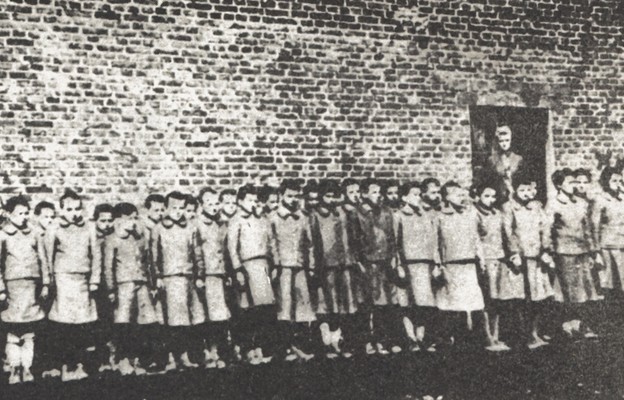 Dziewczęta na tle budynku podobozu dziewczęcego w niemieckim obozie koncentracyjnym dla polskich dzieci przy ul. Przemysłowej w Łodzi, w drzwiach stoi nadzorczyni Eugenia Pol vel Pohl